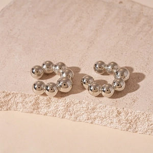 Macro detail of silver C-shaped ear cuffs with metallic bead design on stone texture