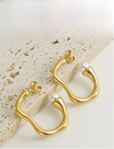 Détail d'une boucle d'oreille irrégulière en or mat ornée d'une perle blanche sur pierre