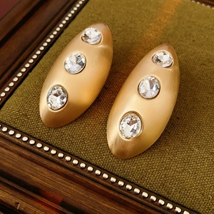 Macro shot of oval gold brushed earrings with sparkling zircons on green velvet