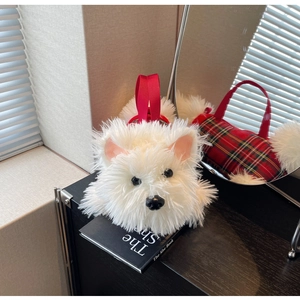 Close-up of white plush Westie dog bag with red strap next to a book and mirror