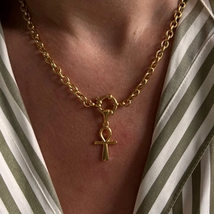 Close-up of golden Ankh cross pendant on thick chain worn by model in green shirt