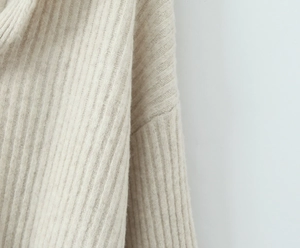 Detailansicht der feinen vertikalen Rippenstruktur und des Strickstoffs am beigen Pullover