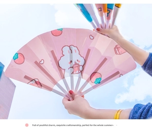 Pink foldable handheld fan with cute bunny illustrations against a clear blue sky
