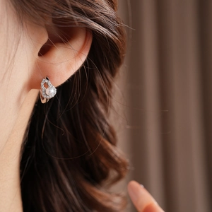 Detail shot of shimmering zircon hollow gourd earring with pearl on model's ear