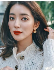 Close-up of a model wearing minimalist golden spherical earrings and a white knit cardigan