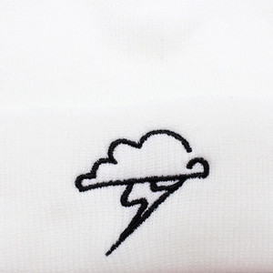 Detail of white ribbed knit beanie with black cloud and lightning bolt embroidery texture