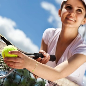 Lifestyle-Foto des 14k Gold Infinity-Armbands mit grünem Edelstein auf dem Tennisplatz