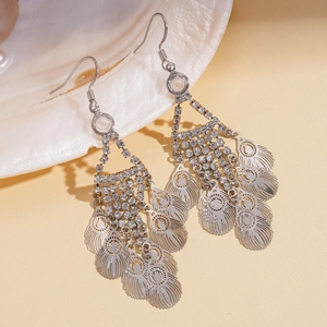Detail view of silver hollow leaf tassel earrings with rhinestones on a seashell