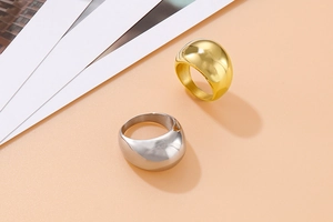 Polished gold and silver dome rings in minimalist stainless steel on a soft neutral surface