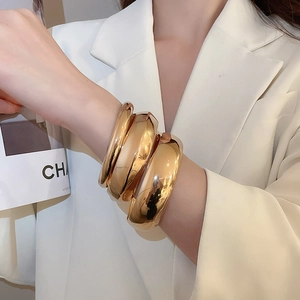 Détail de trois bracelets joncs en métal doré poli portés au poignet pour femme