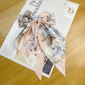 Detail shot of a pink floral satin bow hair clip on a wooden table with a magazine