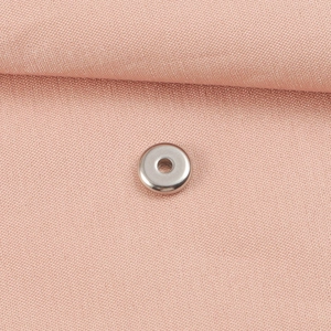 Detailed close-up of a silver stainless steel spacer bead on soft pink fabric texture