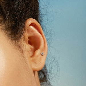 Close-up of 925 sterling silver flower stud earring worn on model against blue sky