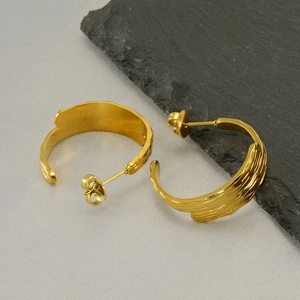 Macro detail of gold-plated hoop earrings with organic hammered texture on stone background