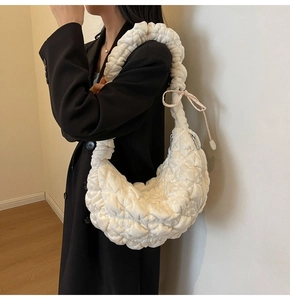Detailed side view of off-white quilted hobo bag with wide pleated strap worn by model