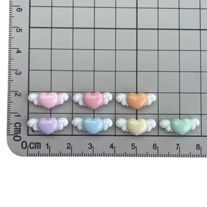 Mini resin winged heart charms in multiple colors for DIY crafts shown on scale mat