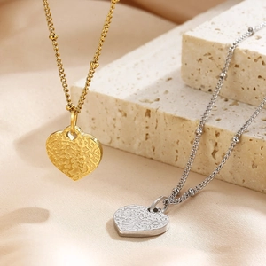 Detail of hammer textured heart pendants in gold and silver on delicate beaded chains