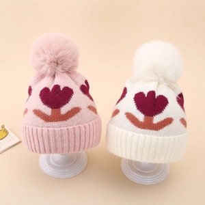 Detailed view of winter baby knit hats with soft faux fur pom-poms and flower patterns