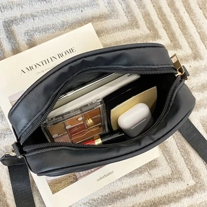 Detail of spacious interior of black crossbody bag with makeup and earphones storage