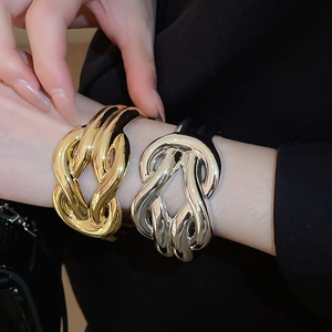 Detailed close-up of stacked gold and silver wide cross-over bracelets with polished finish