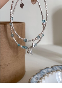 Detail of double-layer beaded bracelet with silver fish pendants and blue pearls