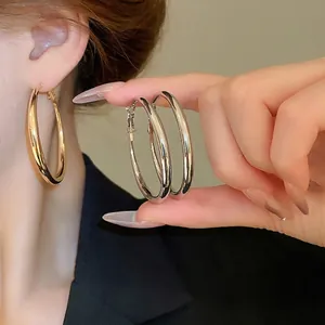 Minimalist large metal hoop earrings in gold and silver finish shown on a female model