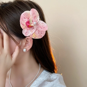 Detail view of pink orchid hair claw with pearl accent worn on model in soft light