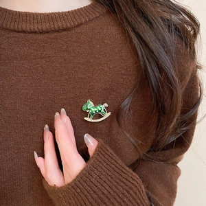 Close-up of green rocking horse brooch with diamonds on a brown knitted sweater