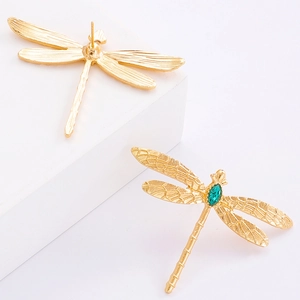 Vue macro de boucles d'oreilles libellule dorées avec cristal vert et ailes ciselées