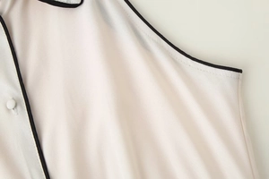 Vue macro d'un col de chemise blanc sans manches avec passepoil noir et boutons en tissu