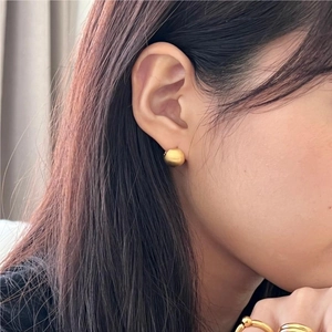 Close-up of minimalist golden matte spherical stud earrings on a model's ear with soft lighting