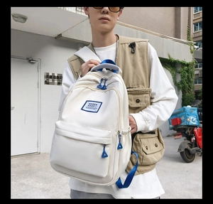 Close-up of white canvas backpack featuring bright blue zipper pulls and brand patch