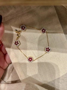 Detail of gold plated bracelet featuring five red zircon flowers on linen fabric