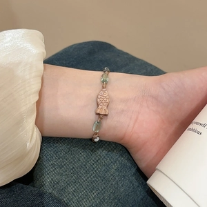 Detailansicht eines gewebten Armbands mit blauen Perlen und einem fischförmigen Metallanhänger