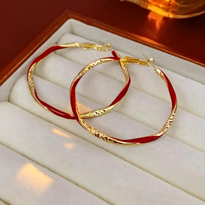 Macro detail of red enamel and gold textured hoop earrings on white velvet fabric