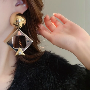 Close-up of golden geometric earrings with rhinestone detail worn by a model