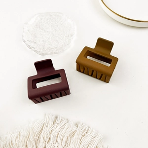 Top view of two matte rectangular hair claws in burgundy and tan colors on a tray