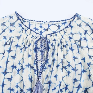 Blusa bianca con stampa geometrica blu, righe dorate e dettaglio scollo in pizzo blu
