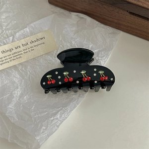 Close-up of black hair claw clip featuring red and green crystal cherry embellishments