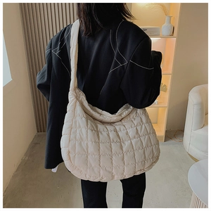 Model wearing a large cream quilted puffer bag with wide strap and zip top closure