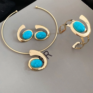 Detail of gold jewelry set featuring oval turquoise stones on a smooth grey surface