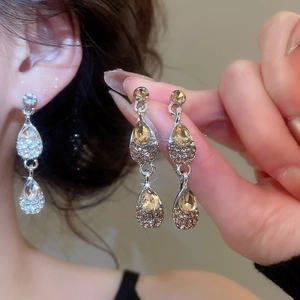 Detail showing water-drop crystal earrings in silver and amber tones worn by a model