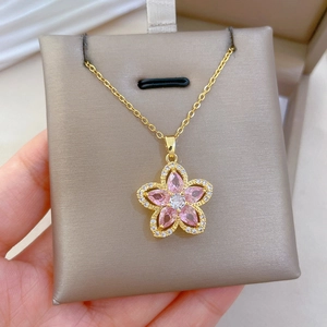 Close-up of gold necklace with pink flower pendant featuring crystals held in hand