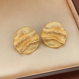 Détail de boucles d'oreilles dorées rondes avec texture ondulée plissée sur du satin