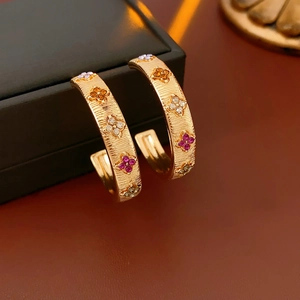 Macro detail of gold C-shaped floral earrings with multi-color crystal inlay on warm background