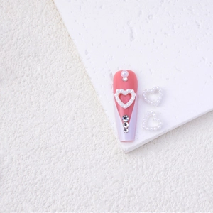 Detail of pink gradient nail art featuring heart-shaped pearls and sparkling rhinestones