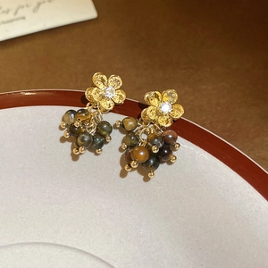 Dettaglio di orecchini floreali dorati con pietre occhio di tigre su un piatto di ceramica