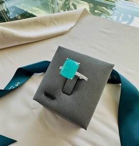 Close-up of a rectangular emerald ring with small diamonds on a grey velvet display