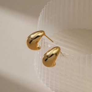 Minimalist 18K gold water drop stud earrings shown on transparent ribbed glass