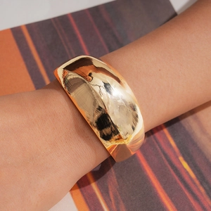 Detail eines minimalistischen polierten goldenen breiten Armreifens am Handgelenk eines Models